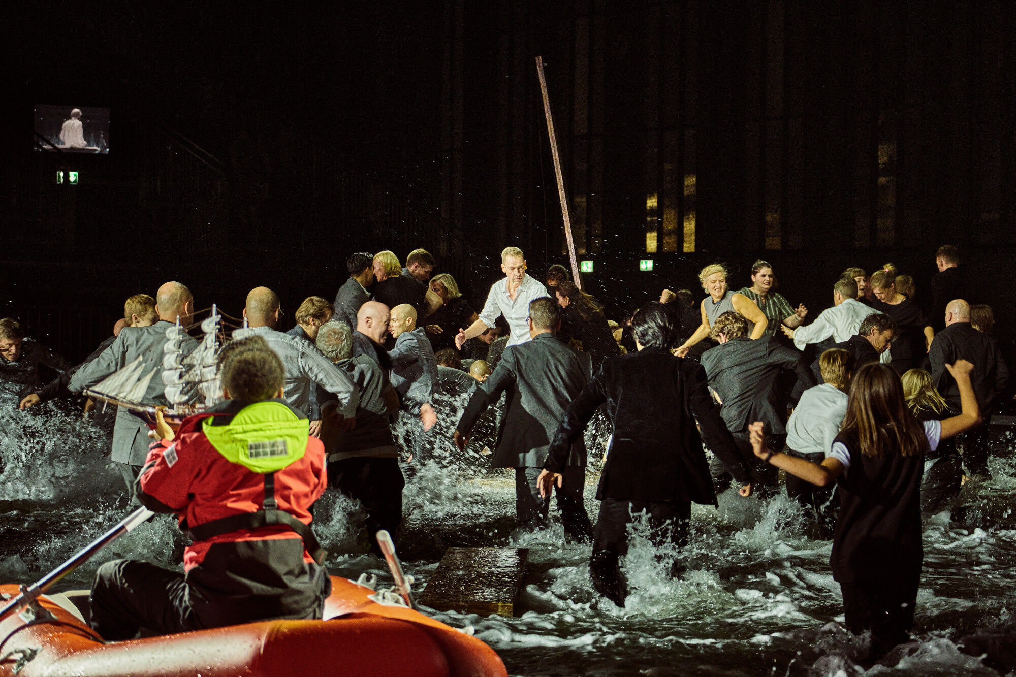 Menschengruppe rettet sich auf ein Floß, im Vordergrund Rettungsbot mit Sanitäterin