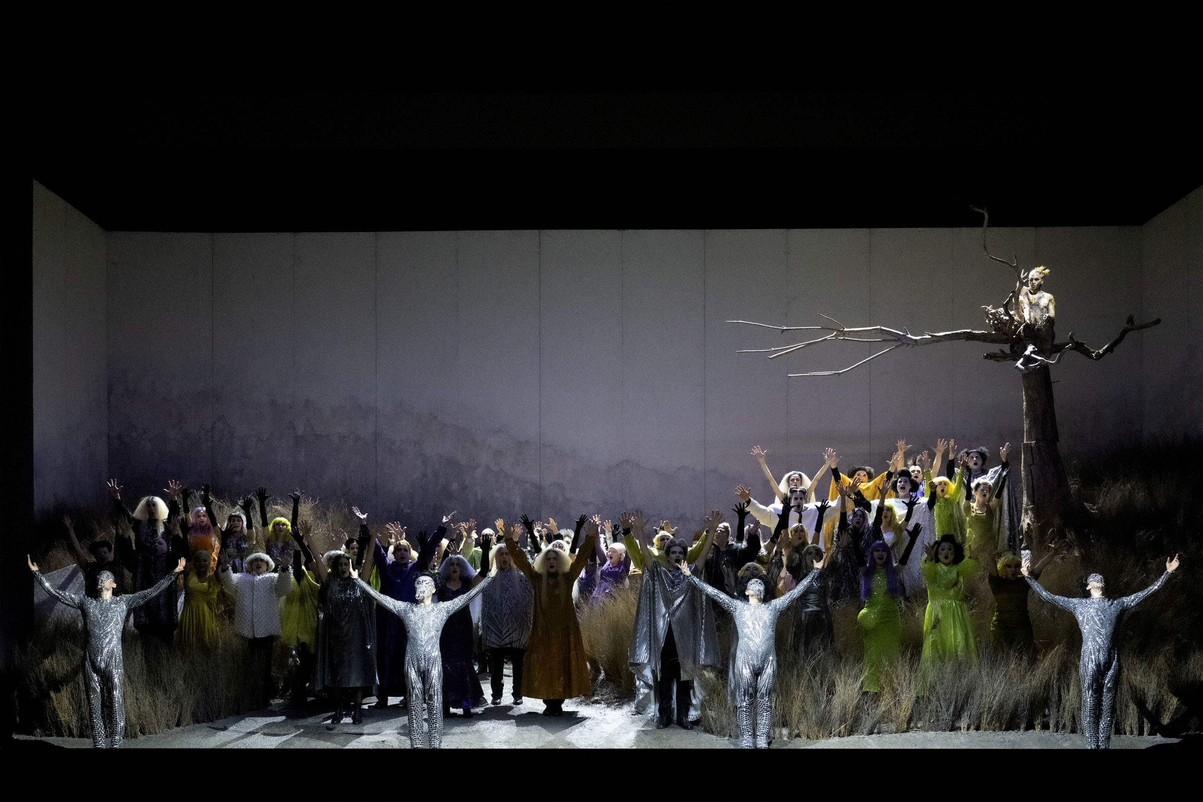 Viele Darsteller:innen auf der Bühne, rechts ein Baum ohne Blätter, darauf sitzend Figur goldener Hahn